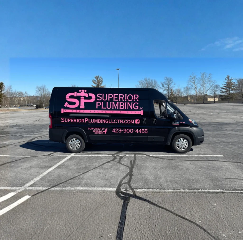 Black Superior Plumbing van with pink logo and text, parked in an empty asphalt lot under a clear blue sky